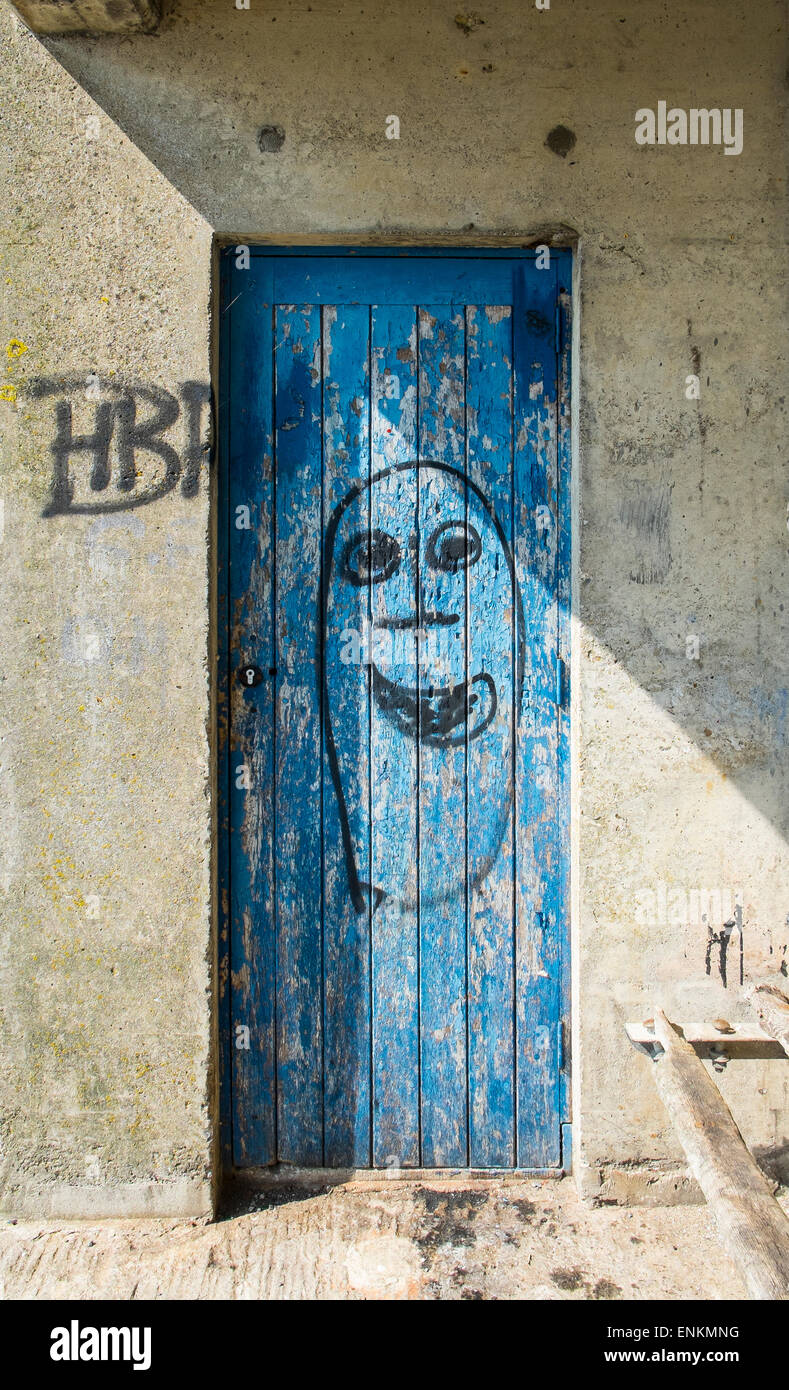 Una porta con peeling vernice blu e faccia primitivi graffiti Foto Stock