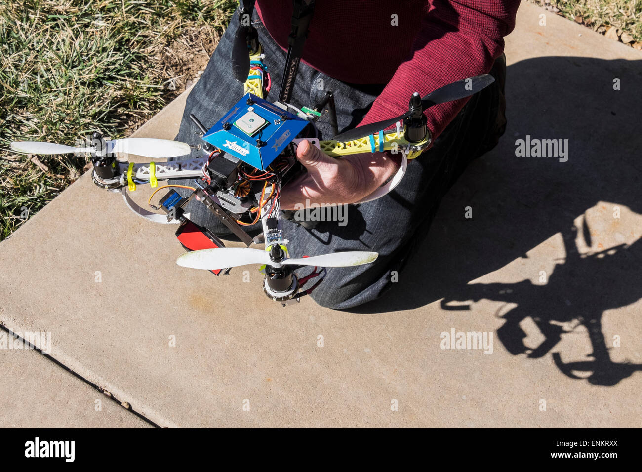 Un uomo si inginocchia su un marciapiede e mantiene il suo progetto DIY quad copter drone. Foto Stock