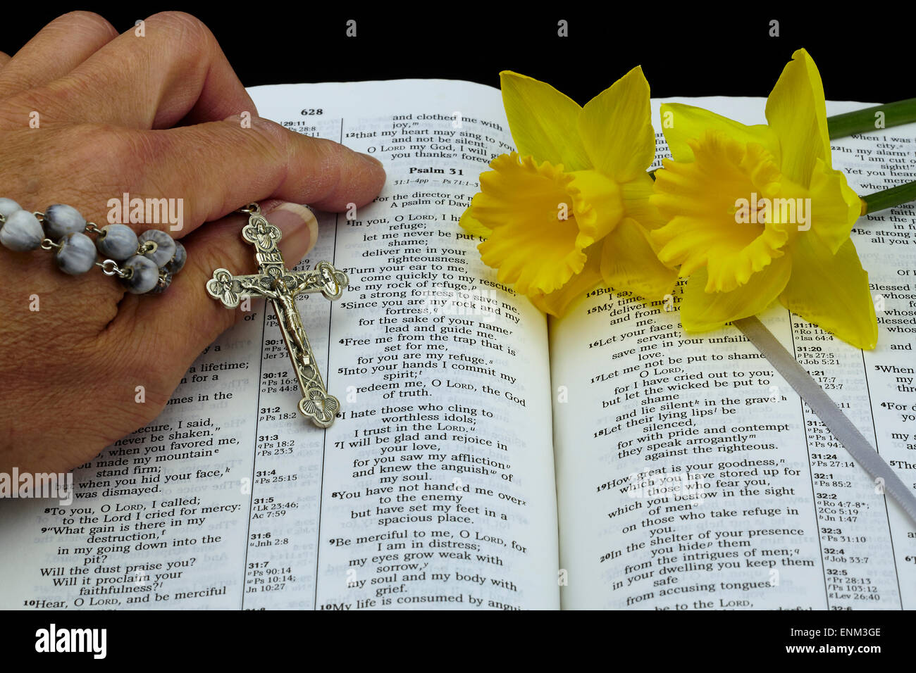 Uomo con lavori di vintage lacrime rosario tallone e argento crocifisso rivolta ai salmi nella Bibbia aperta e daffodil fiori Foto Stock
