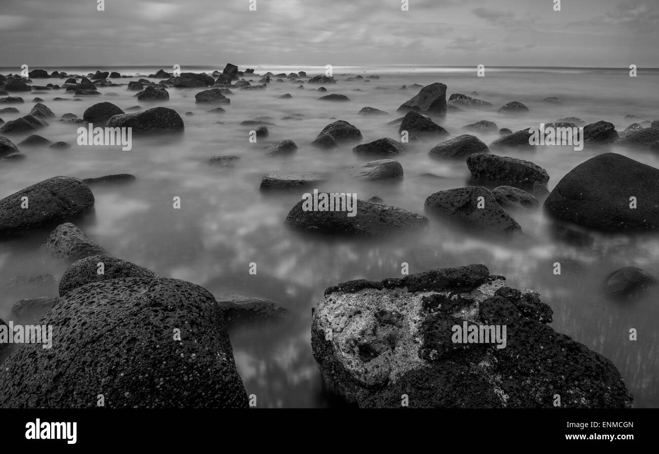 Moody in bianco e nero lunga esposizione di onde che si muove intorno un roccioso litorale vulcanico. Foto Stock