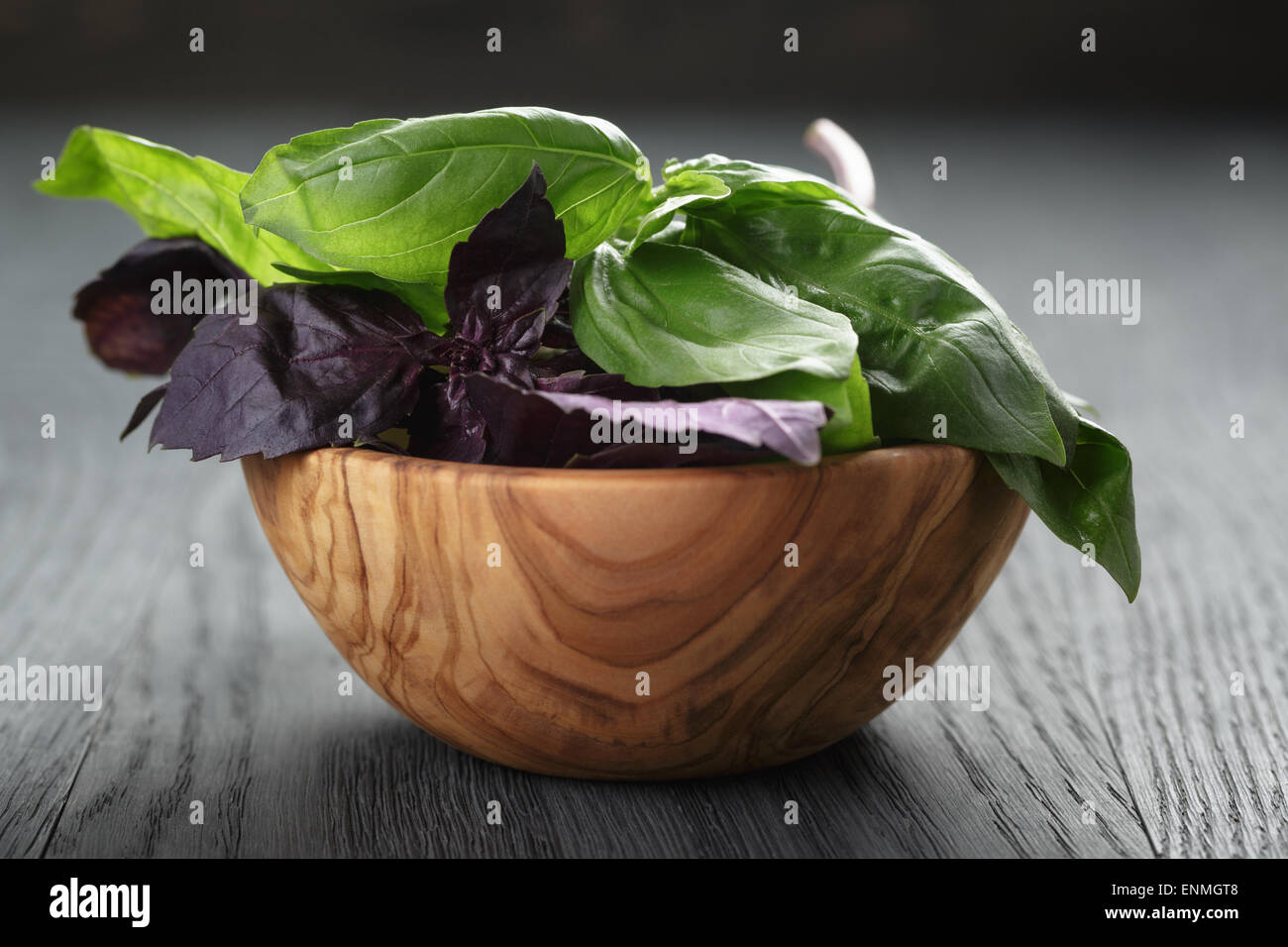 Verde e viola le foglie di basilico in ciotola di legno su un tavolo di legno Foto Stock