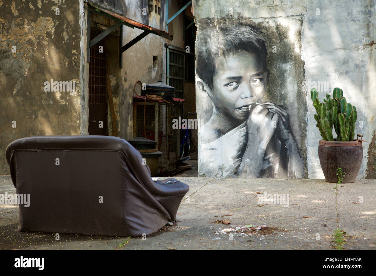 Meglio di TV; sedersi nel vecchio divano posto su una strada pubblica con una vista di alcuni arte di strada. Grande la foto di un bambino asiatico mangiare Foto Stock