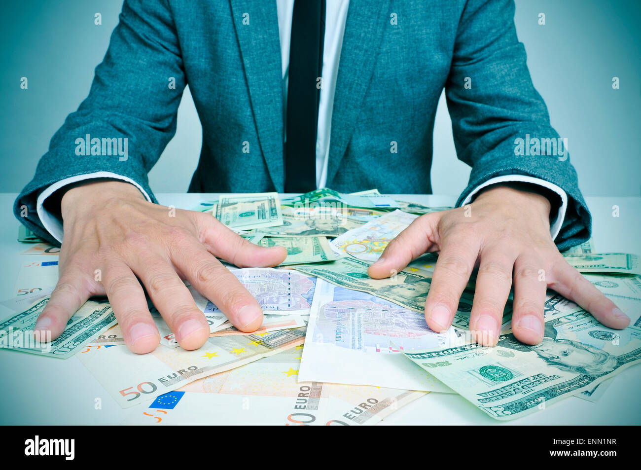 Primo piano di un giovane uomo caucasico in tuta seduto alla sua scrivania piena di euro e le fatture del dollaro cercando di tenerli, raffiguranti Foto Stock
