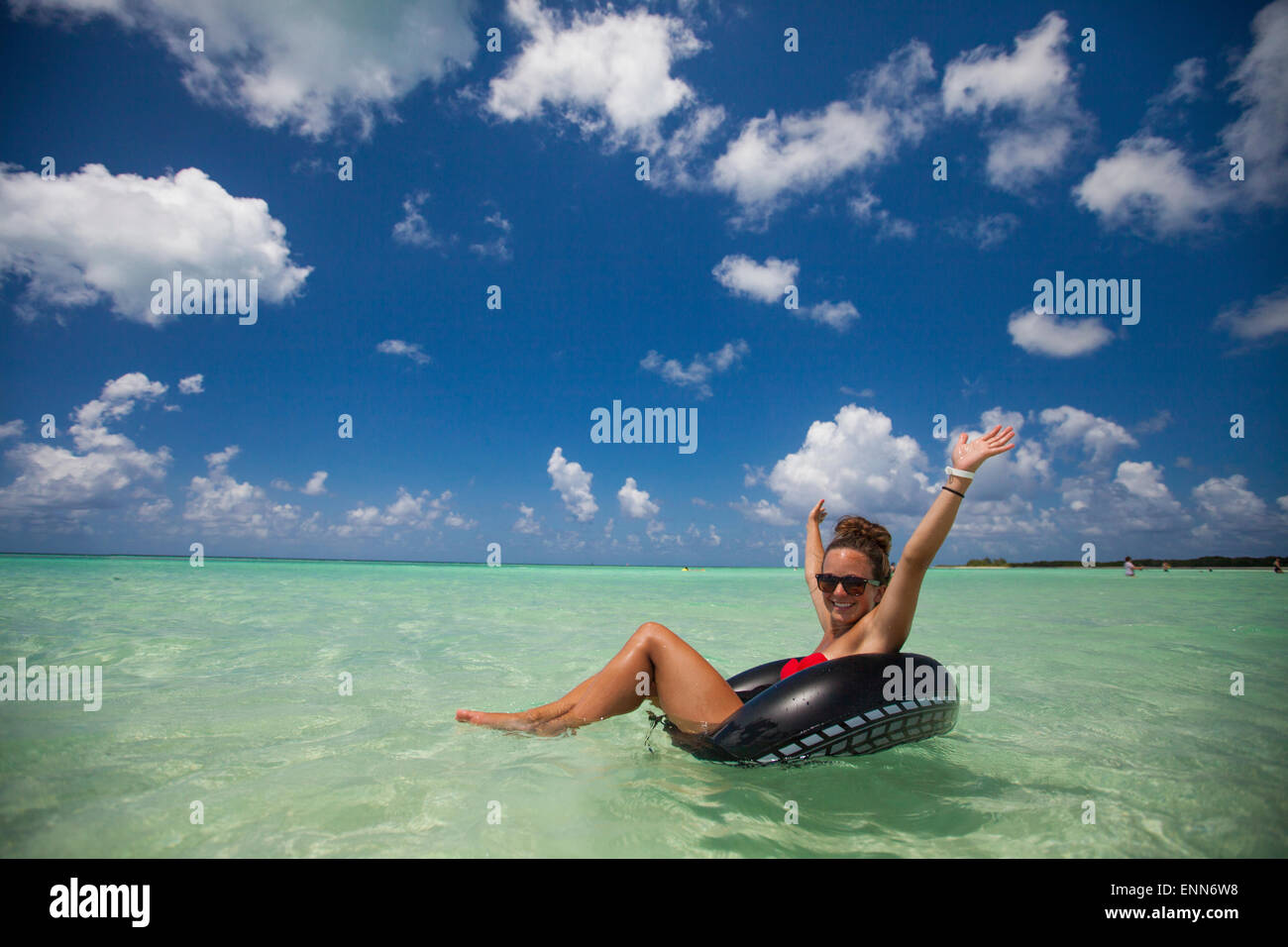 Una giovane donna che indossa un bikini galleggia su un tubo gonfiabile in acque turchesi mentre è in vacanza in Cayo Coco, Cuba. Foto Stock