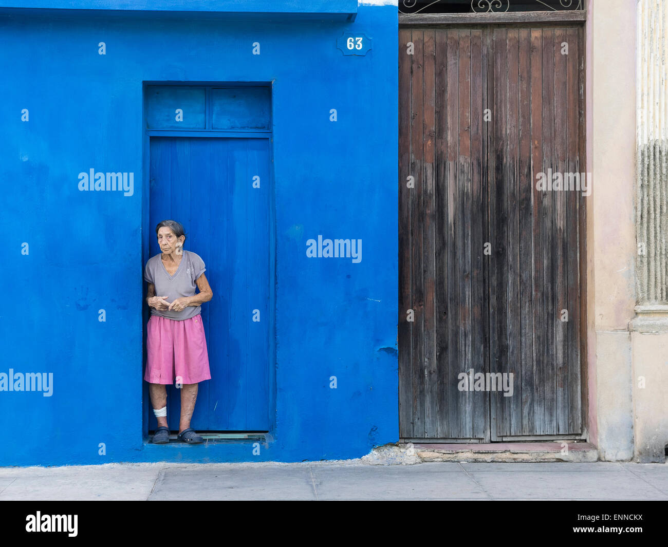 Un ispanico senior citizen sorge nella porta di un blu profondo cercando di parete triste in Santiago de Cuba. Foto Stock