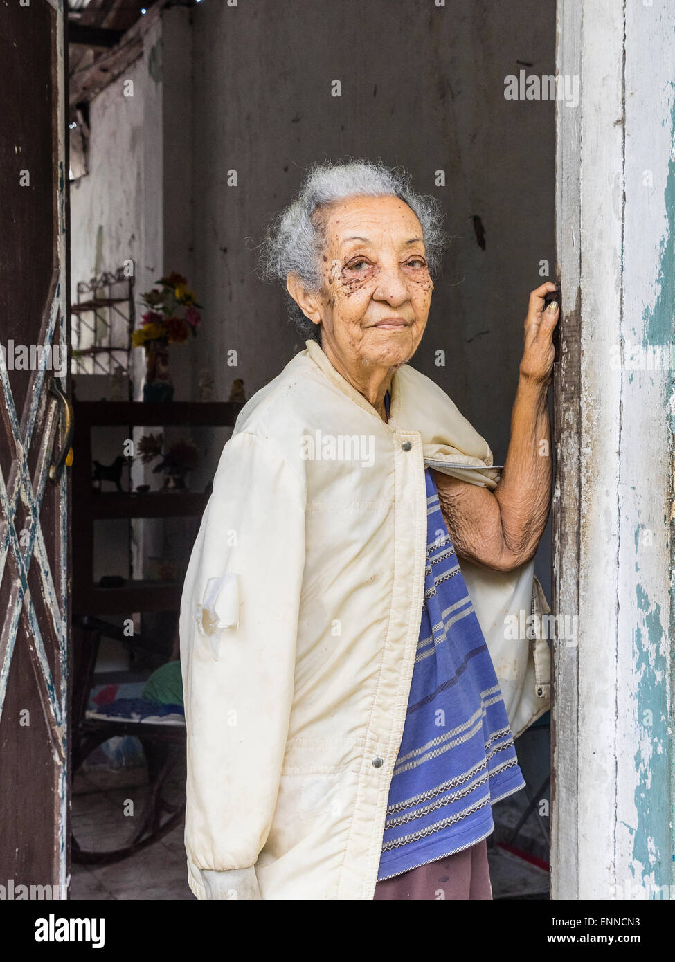 Afro-cubane femmina senior citizen con capelli grigi in piedi sulla porta della sua casa guardando fuori, un braccio contro la porta Foto Stock