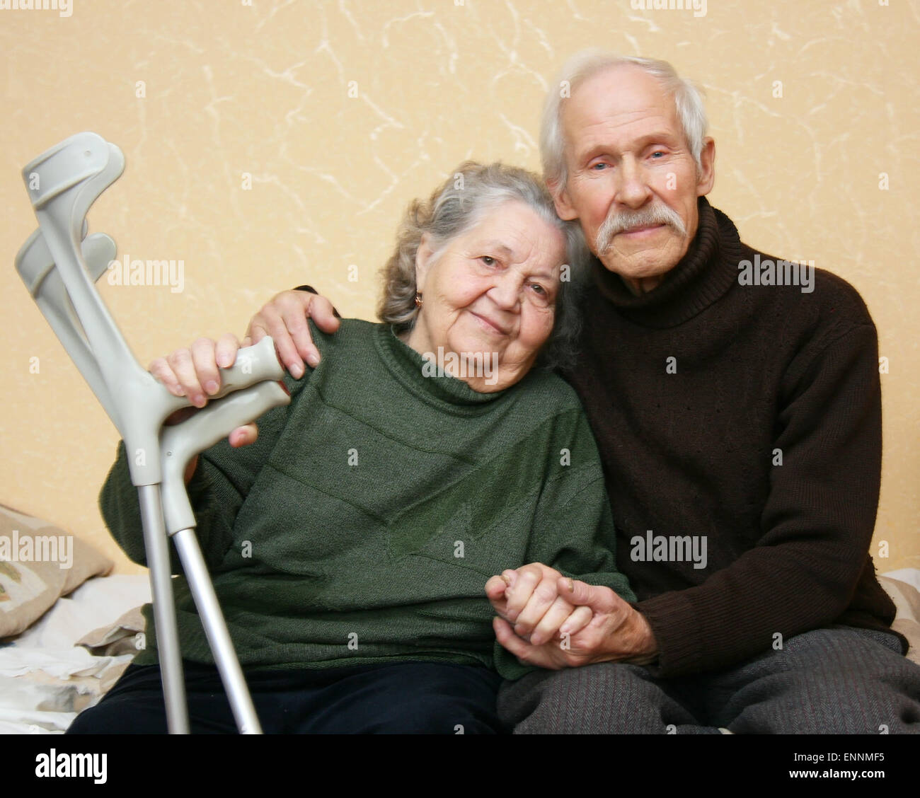 Il nonno in un maglione scuro che dolcemente abbracciano la nonna che lo tiene in braccio stampelle Foto Stock