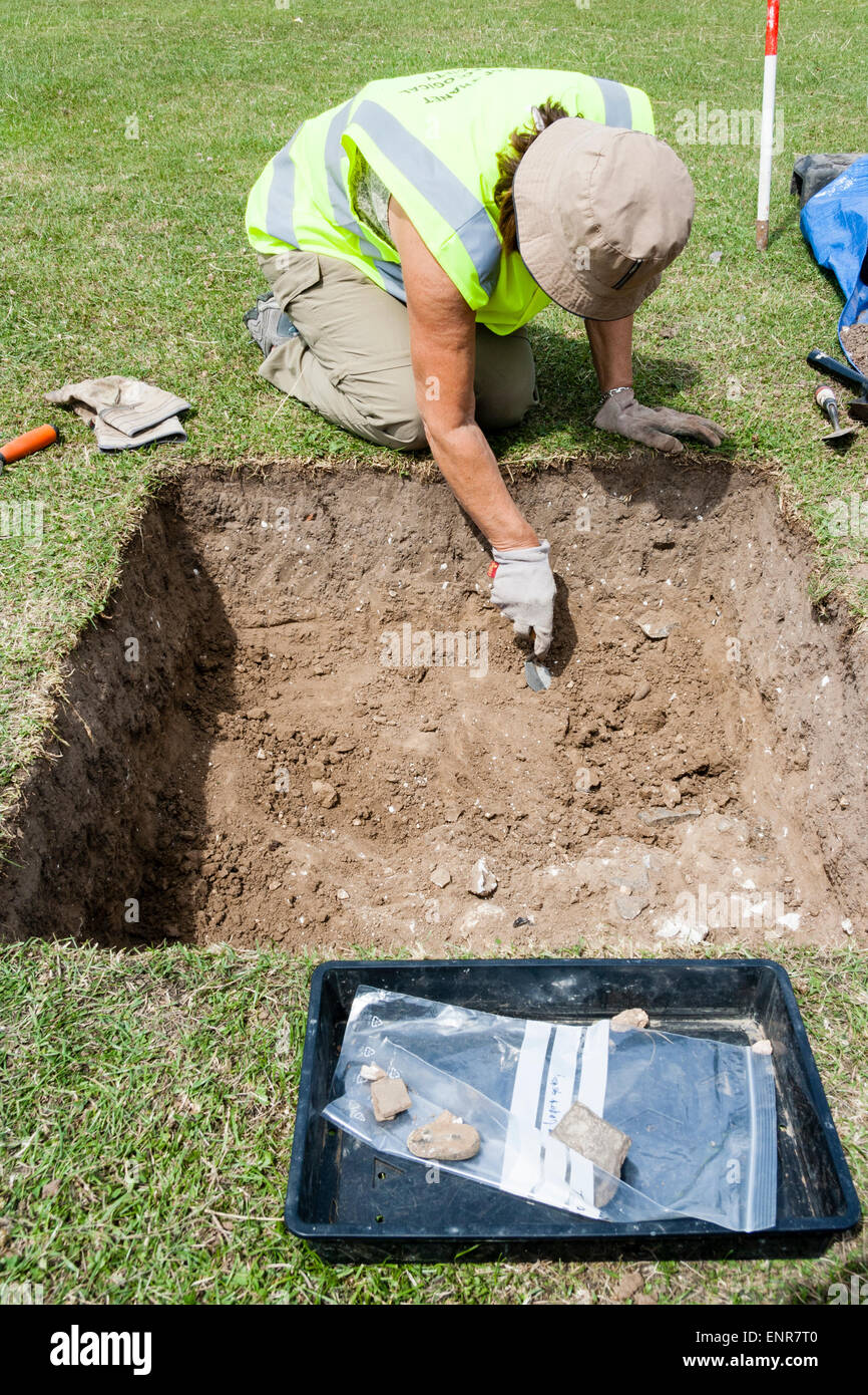 Archeologo scavare trincea romana con cazzuola durante uno scavo. Inginocchiarsi sul bordo del fosso e inclinarsi verso il basso allontanando delicatamente lo sporco Foto Stock