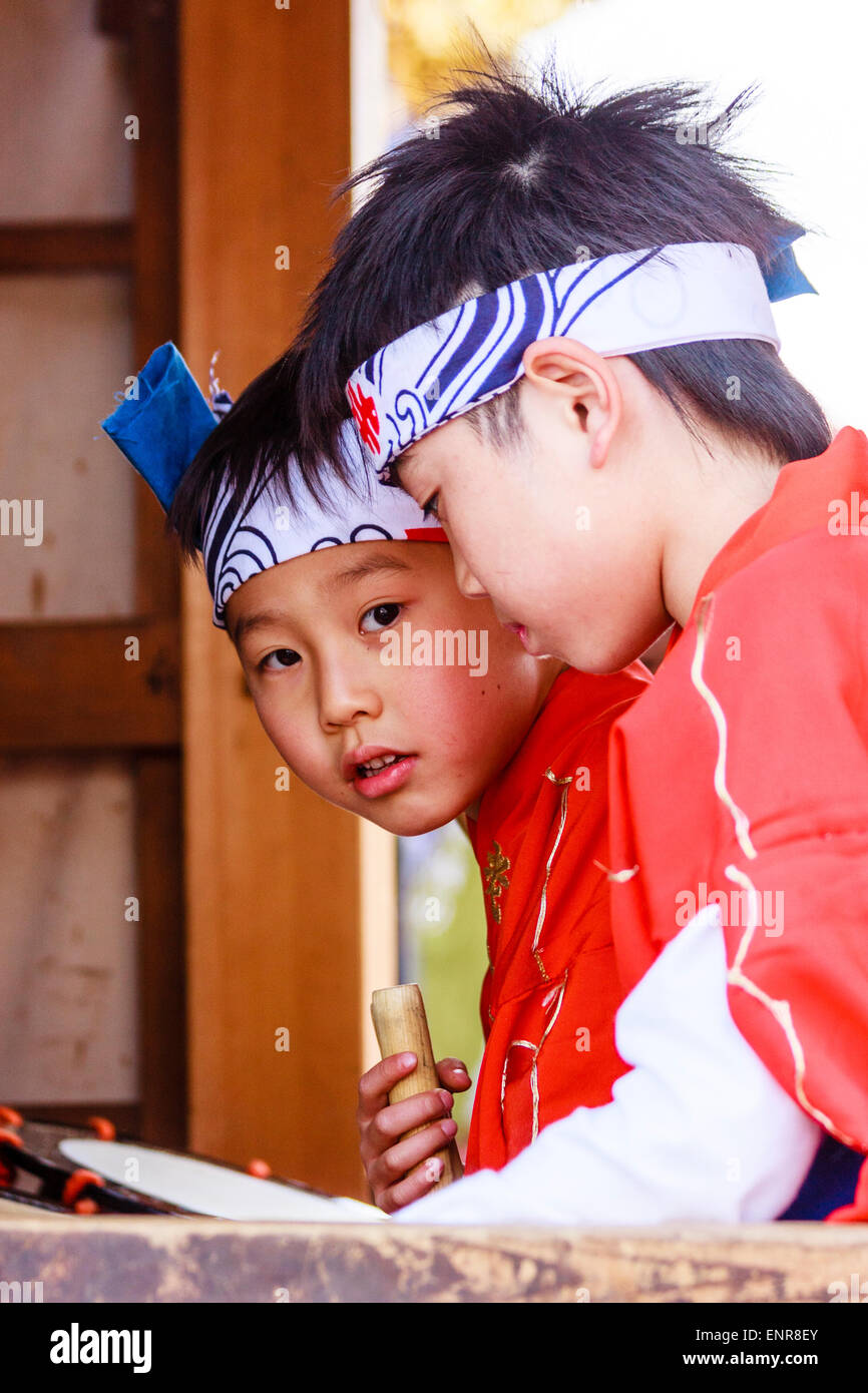 Due bambini giapponesi, ragazzi di 9-10 anni, con archetto e costume rosso che chiacchiera mentre si siede in uno yama, galleggiamento di carnevale, un fotografo di avvisi. Foto Stock