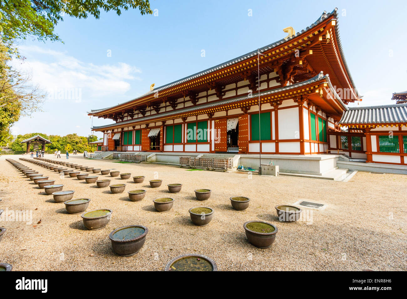 Fila di ciotole piene d'acqua di fronte alla sala bianca e vermiglio Daikodo al tempio Yakushi a Nara. Sfondo blu cielo. Foto Stock