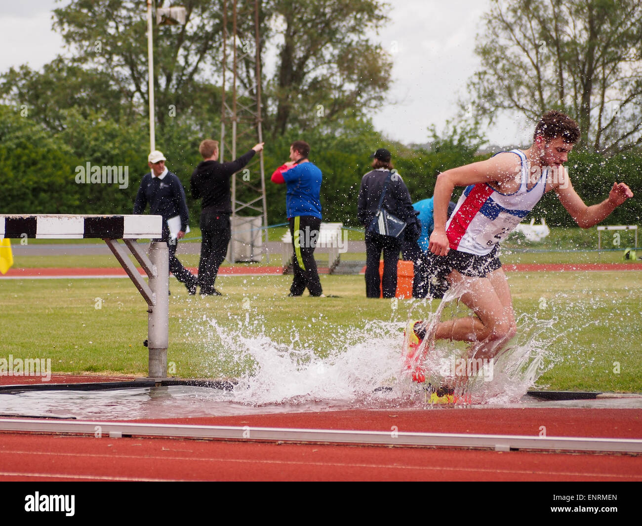 Matthew Smith della città di Portsmouth club atletica schizzi attraverso il salto in acqua durante la steeple chase evento. Foto Stock
