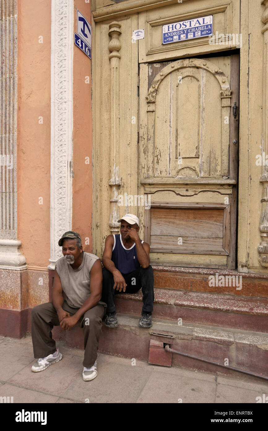 Gli uomini in appoggio sulle porte del vecchio edificio con camere in affitto, Trinidad, Cuba Foto Stock