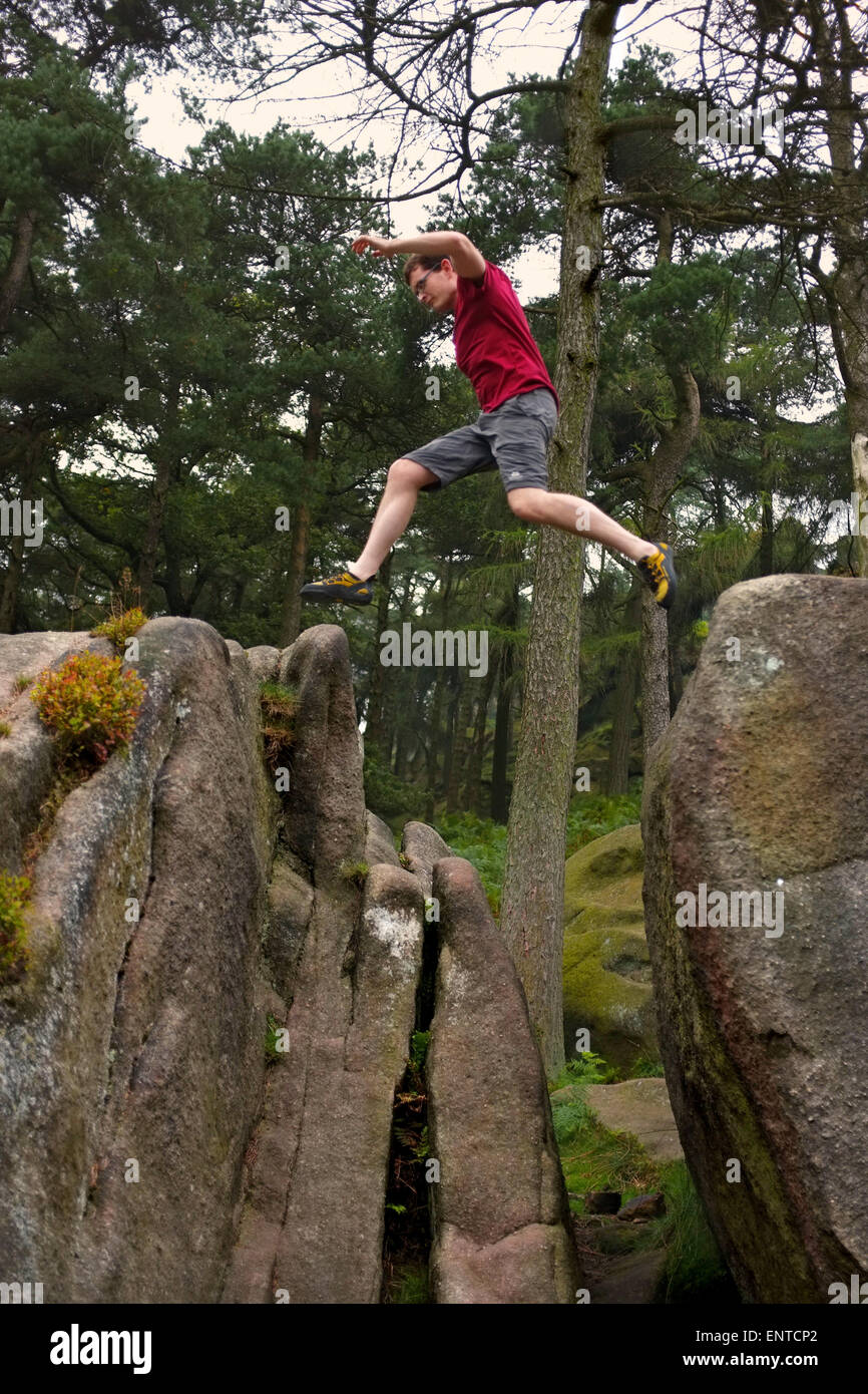 Giovane uomo di saltare attraverso un divario tra le rocce Foto Stock