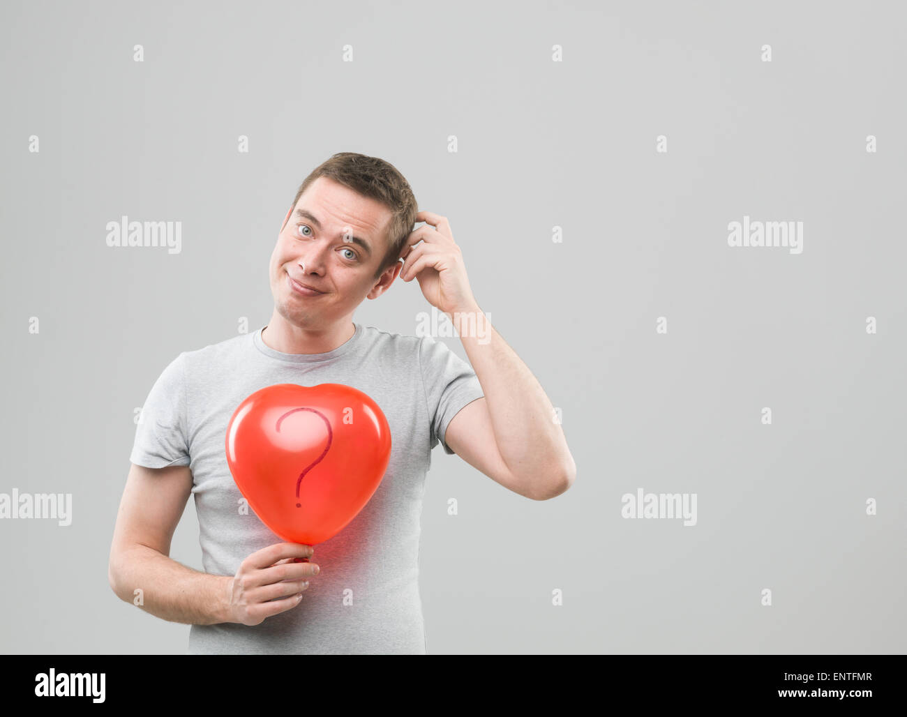 Giovane uomo caucasico di contenimento a forma di cuore palloncino con punto interrogativo, pensando gesto. copia di spazio disponibile Foto Stock