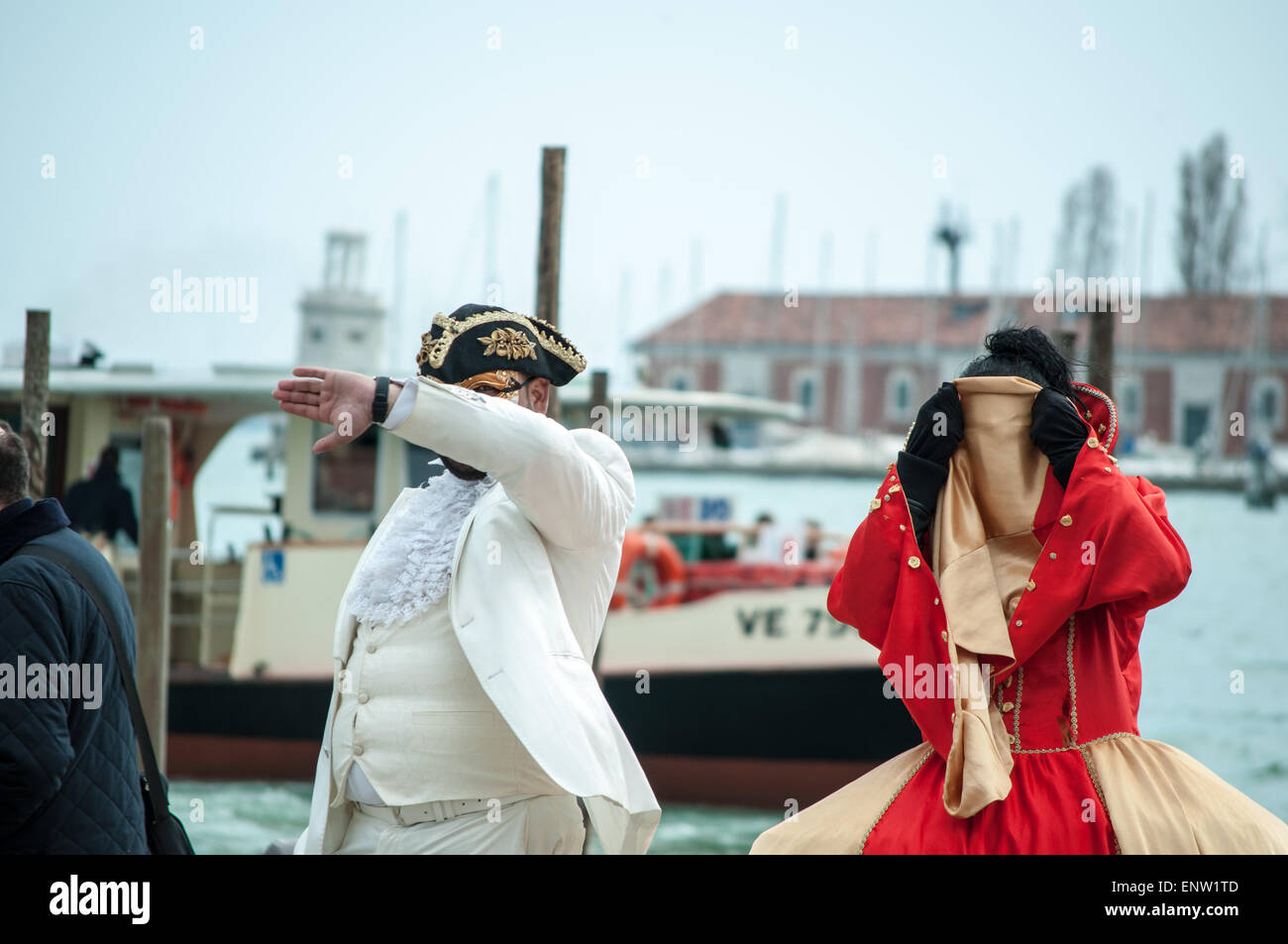 Due artisti di strada, maschio e femmina, vestito come commedia dell'arte personaggi nascosti dalla fotocamera su una strada di Venezia Foto Stock