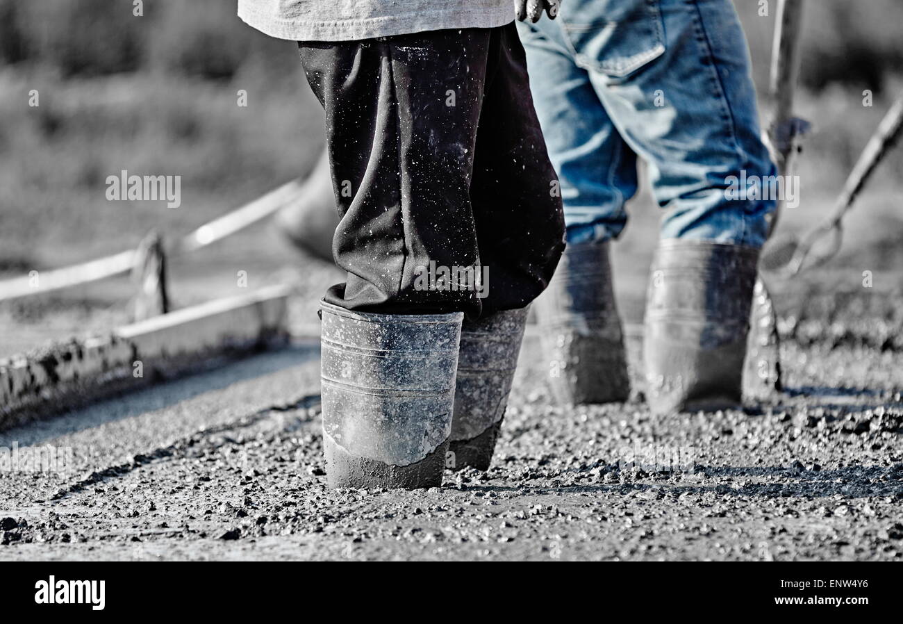 Costruzione in muratura di cemento i lavoratori uomini in scarpe pesanti lavorare nel nuovo calcestruzzo bagnato. Foto Stock
