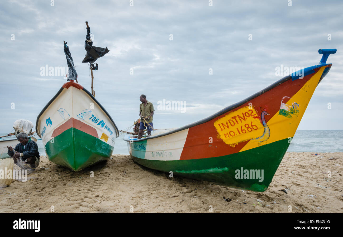 Indian fisherman tendendo le loro reti da parte loro barche sulla spiaggia di Marina, Chennai, India Foto Stock