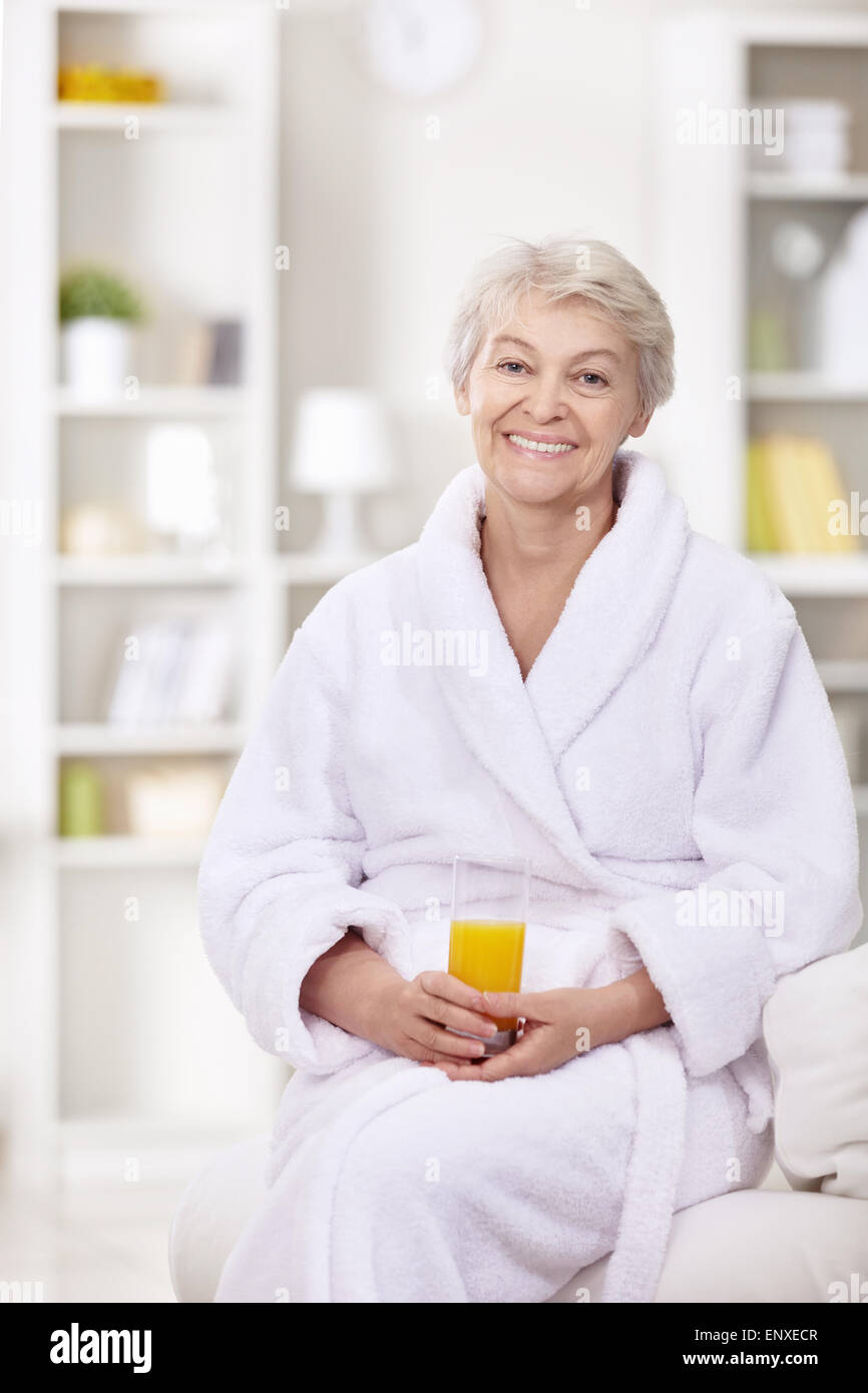 Una donna anziana in una veste bianca con un bicchiere di succo di frutta Foto Stock