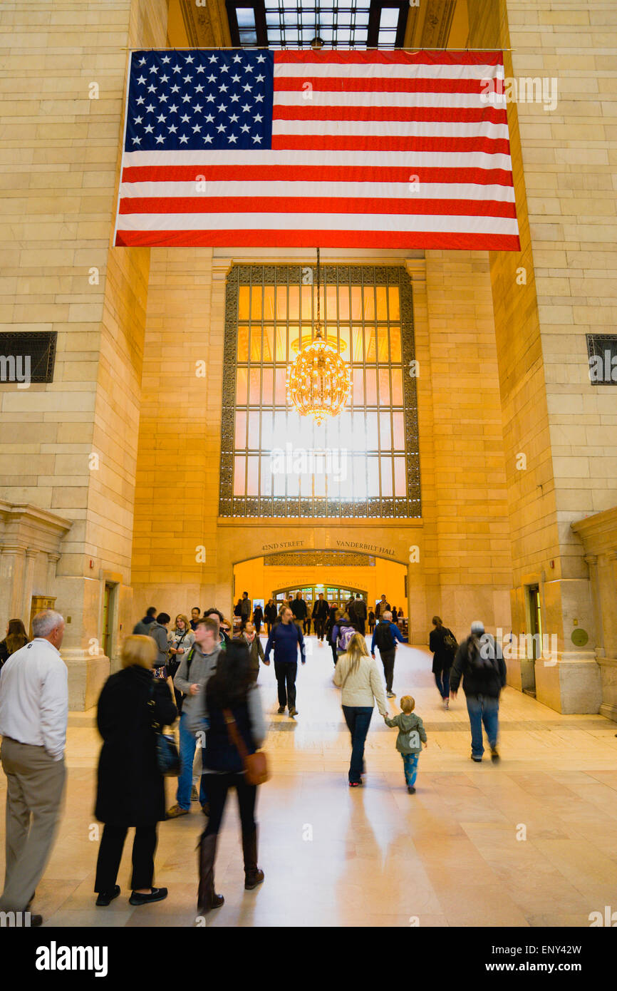 Stati Uniti d'America, New York Manhattan, Grand Central Terminal atrio principale occupato con le persone e le stelle e strisce di bandiera a penzoloni al di sopra di loro. Foto Stock