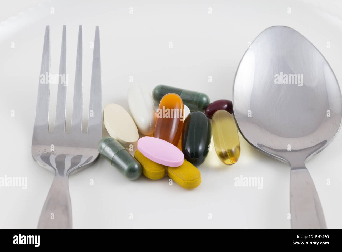 Più pillole di farmaco su un piatto e cucchiaio e forchetta su bianco Foto Stock