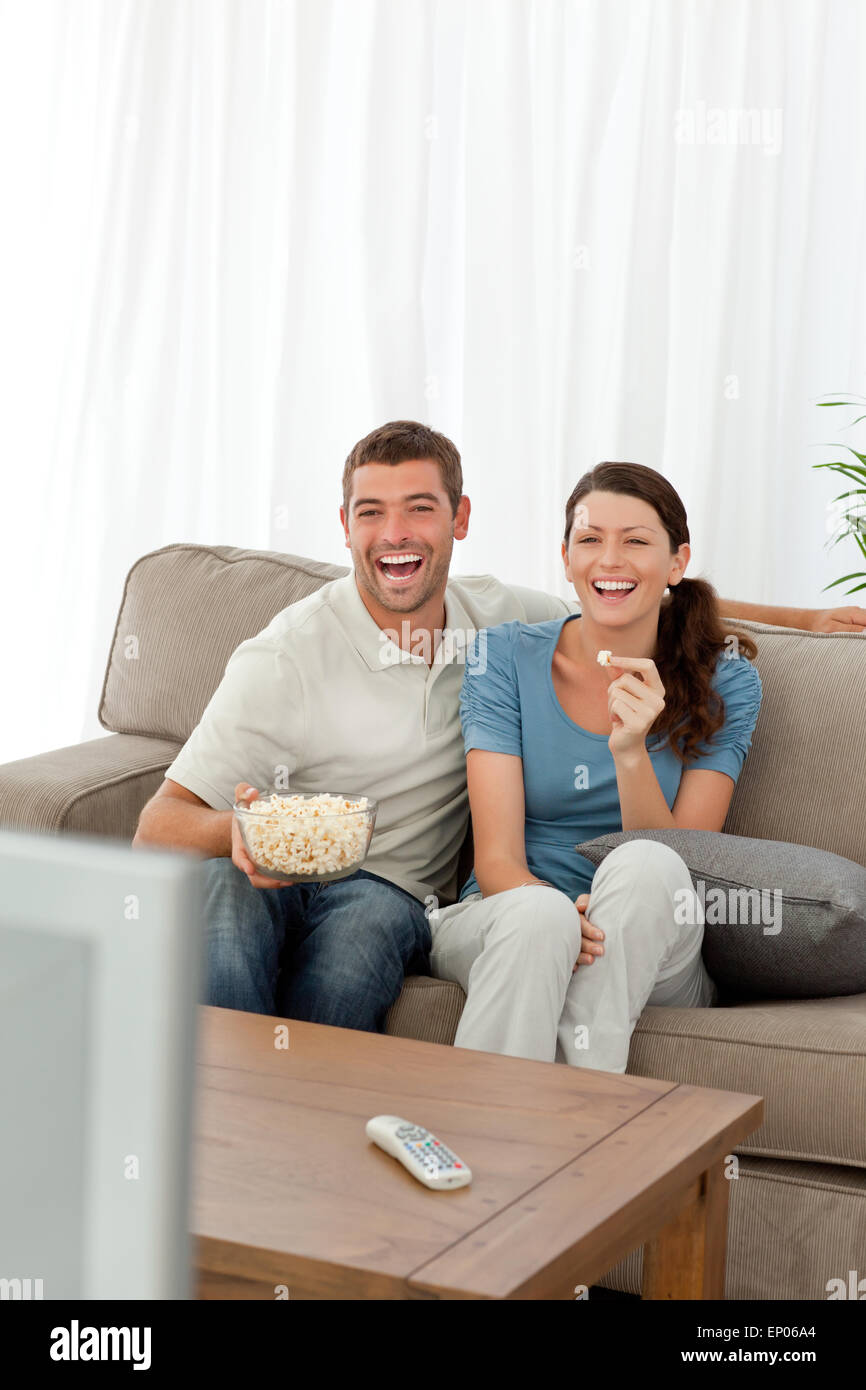 Carino coppia mangiare pop corn mentre guardano la televisione sul divano Foto Stock