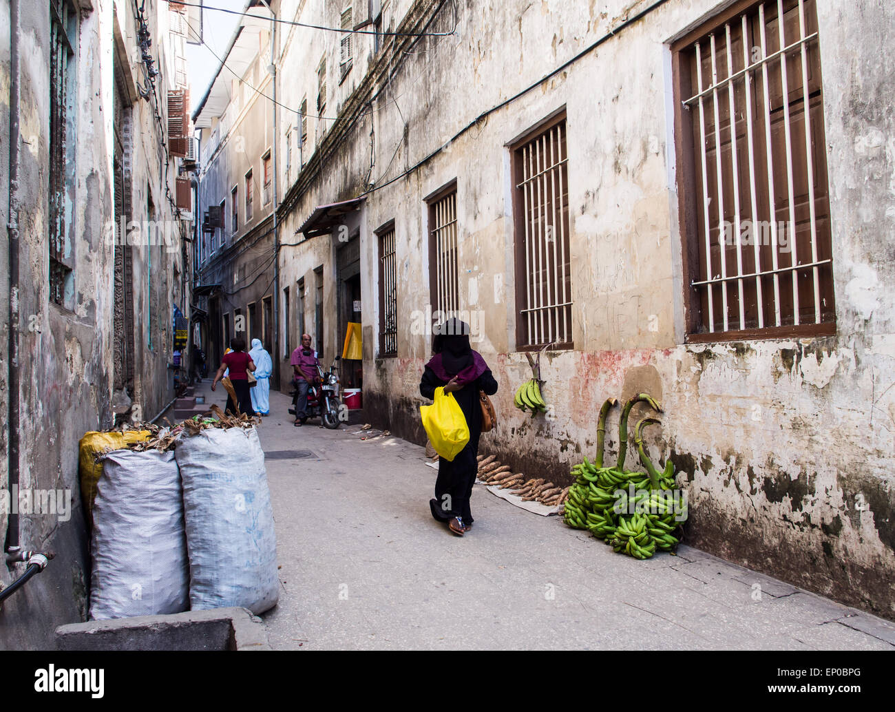 La popolazione locale a camminare su una delle strade strette nella parte vecchia della città di pietra, Zanzibar in Africa orientale. Orientamento orizzontale Foto Stock