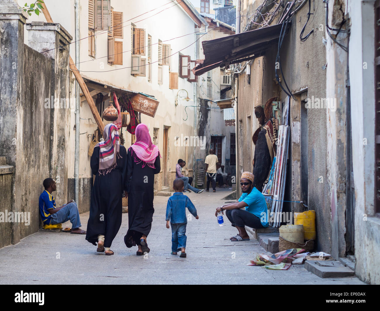 La popolazione locale a camminare su una delle strade strette nella parte vecchia della città di pietra, Zanzibar in Africa orientale. Orientamento orizzontale Foto Stock
