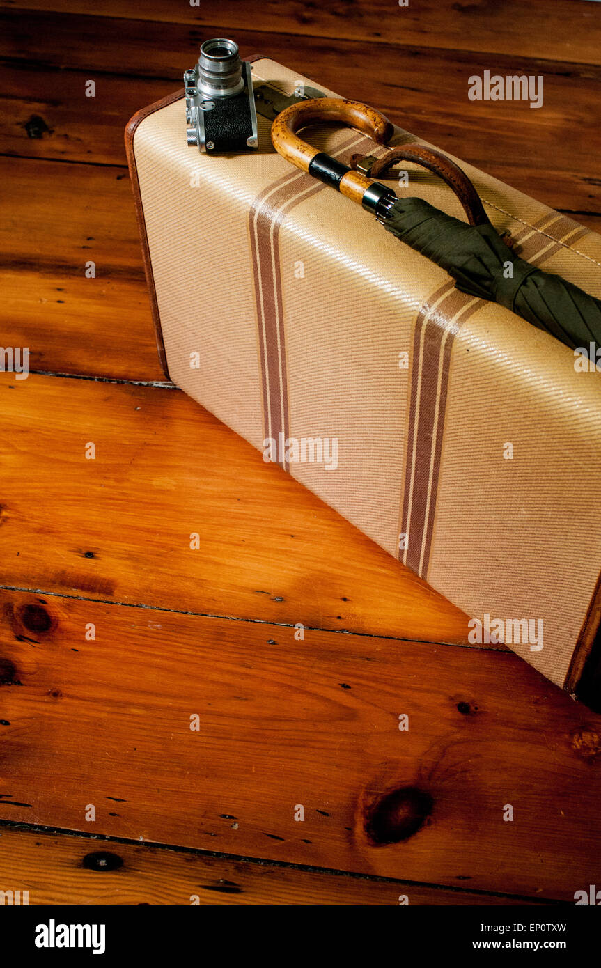 Una valigia vintage, fotocamera e ombrello a sedersi su un pavimento di legno. Foto Stock