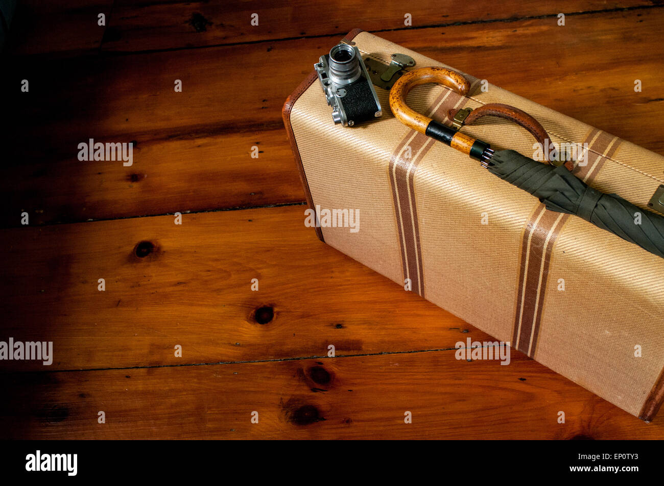 Una valigia vintage, fotocamera e ombrello su un pavimento di legno. Foto Stock