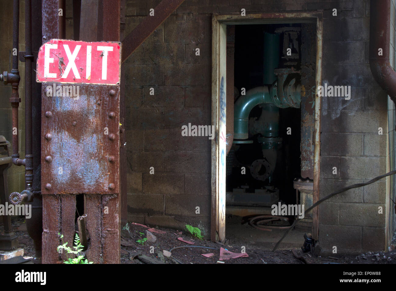 Segnale di uscita sul palo arrugginito con interno di abbandono di sito industriale attraverso la porta. Foto Stock