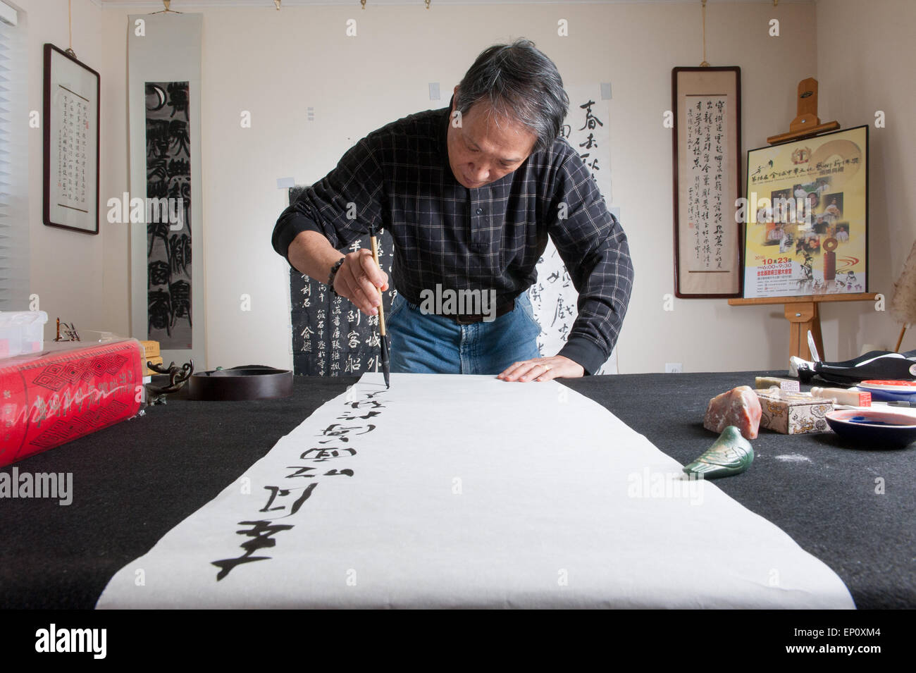 Uomo asiatico usando un pennello per dipingere la calligrafia cinese su un grande foglio di carta bianca in Gaithersburg, Maryland. Foto Stock