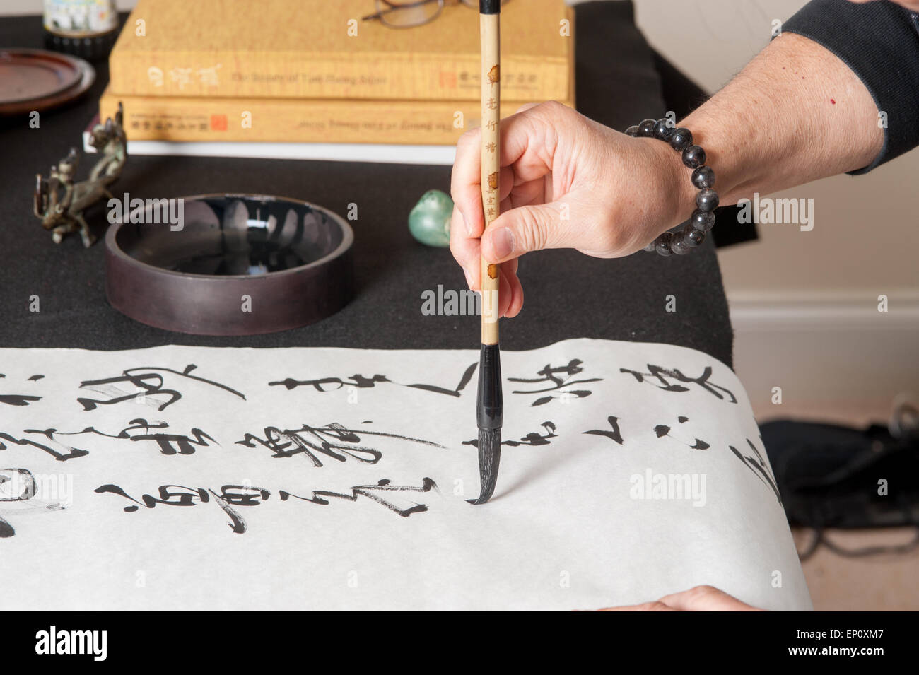 Mano d'uomo utilizzando un pennello per dipingere la calligrafia cinese su un grande foglio di carta bianca in Gaithersburg, Maryland. Foto Stock