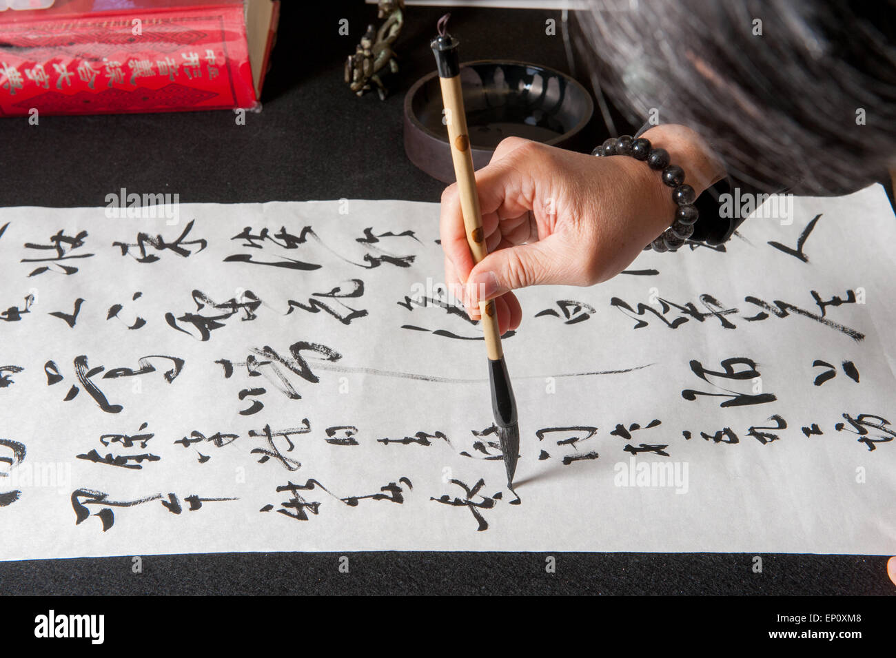 Mano d'uomo utilizzando un pennello per dipingere la calligrafia cinese su un grande foglio di carta bianca in Gaithersburg, Maryland. Foto Stock