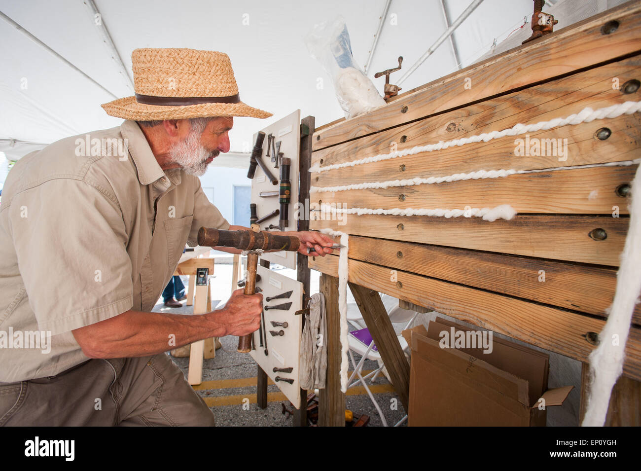 Uomo in cappello di paglia utilizzando gli strumenti tradizionali di spingere il cotone tra assi di legno a Baltimore, Maryland, Stati Uniti d'America Foto Stock