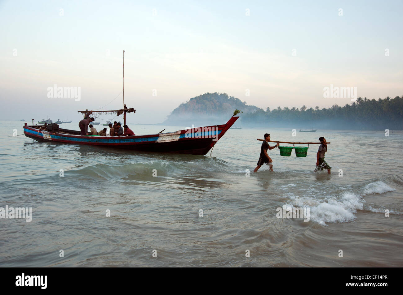 Due pescatori scaricano ceste di pesce dalle loro barche da pesca ormeggiate sulla spiaggia di Ngapali all alba del Myanmar Foto Stock