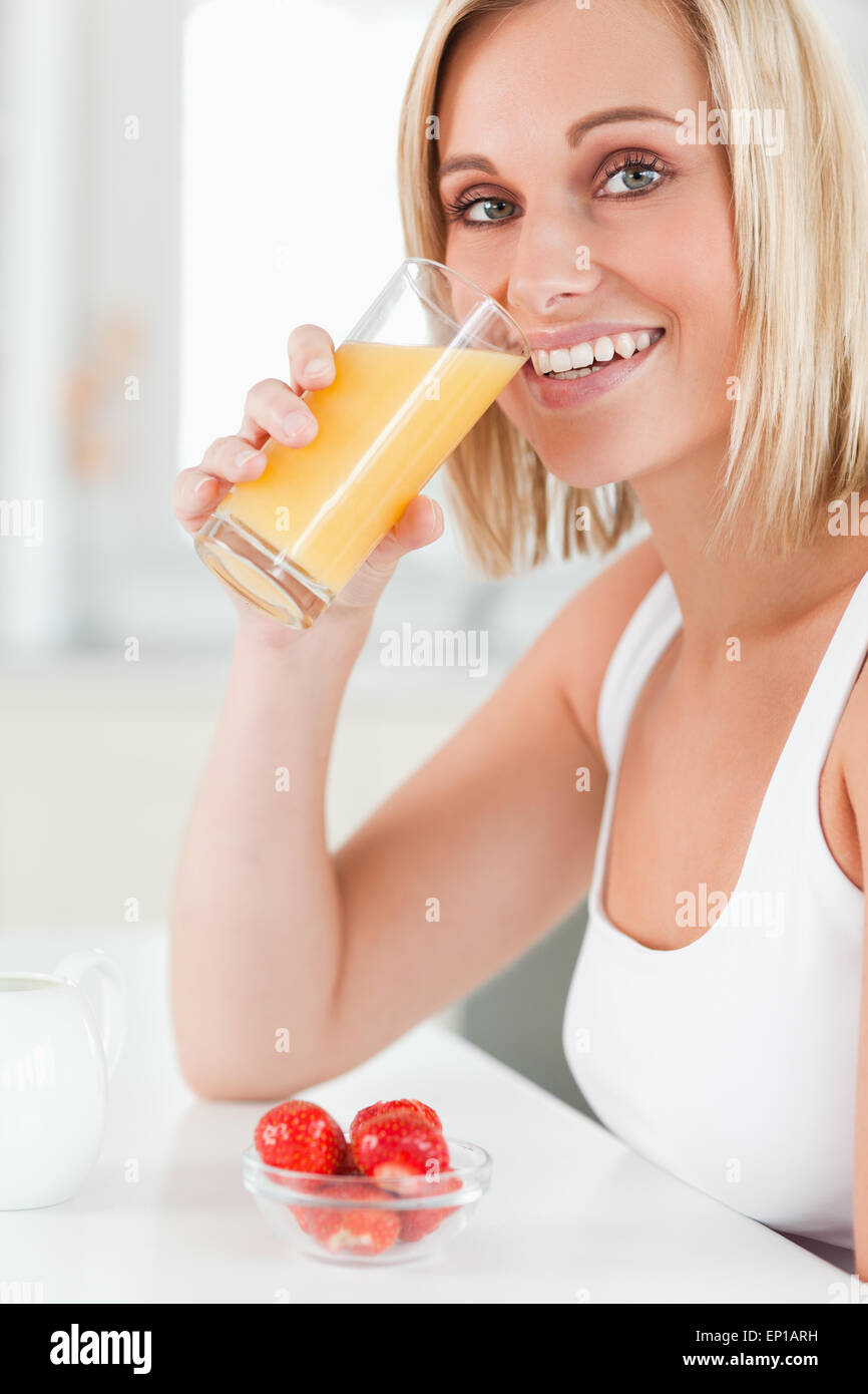 Donna di bere un bicchiere di succo di arancia sorridente verso la telecamera Foto Stock