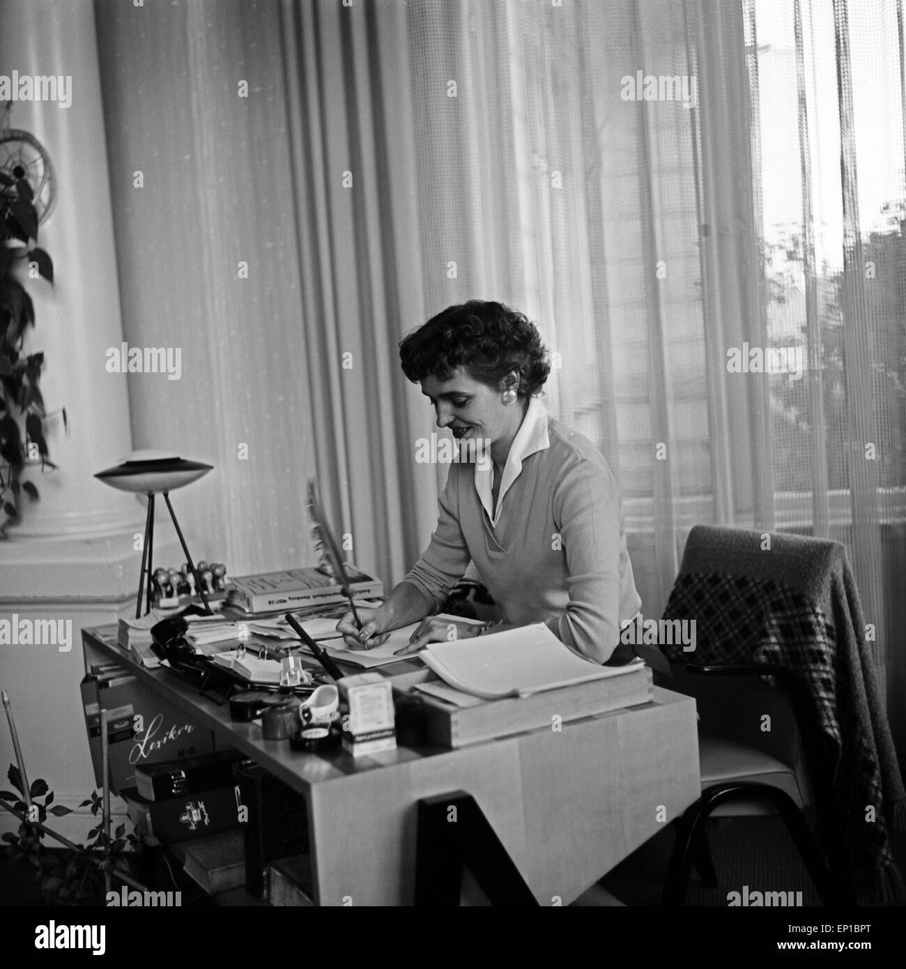 Eine Frau sitzt am Schreibtisch und schreibt mit einer Feder, Deutschland 1950er Jahre. Una donna seduta alla sua scrivania e la scrittura Foto Stock