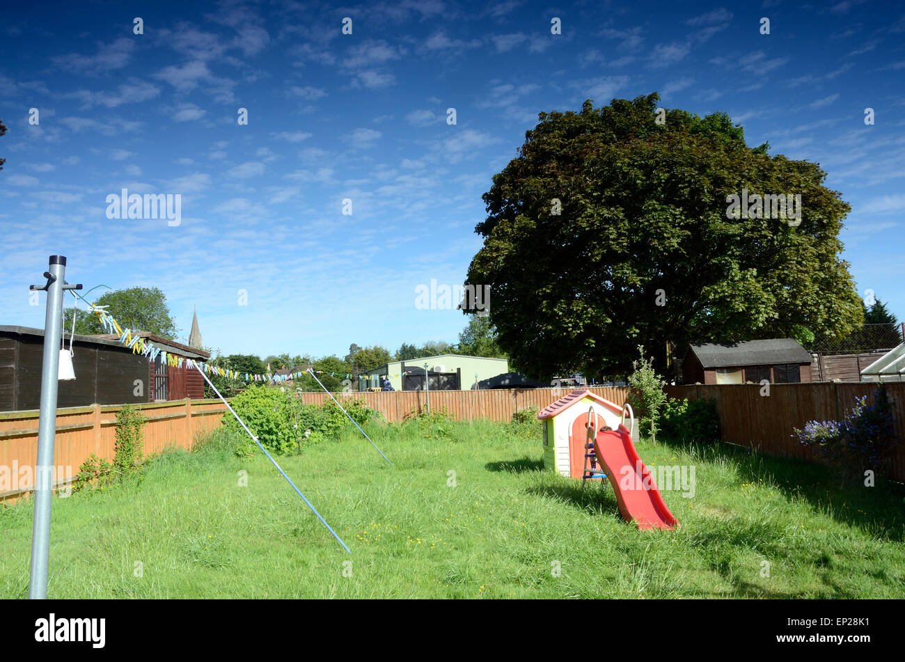 Una vista di un giardino sul retro con ricoperta di erba, una linea di lavaggio, un gioco del bambino casa e una slitta. Foto Stock