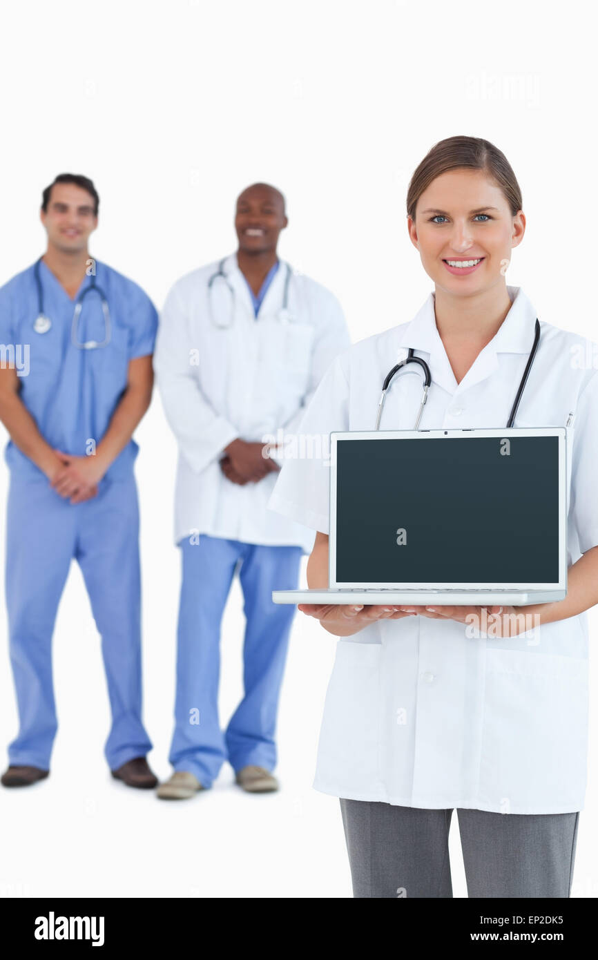 Sorridente medico mostra portatile con i colleghi dietro di lei Foto Stock