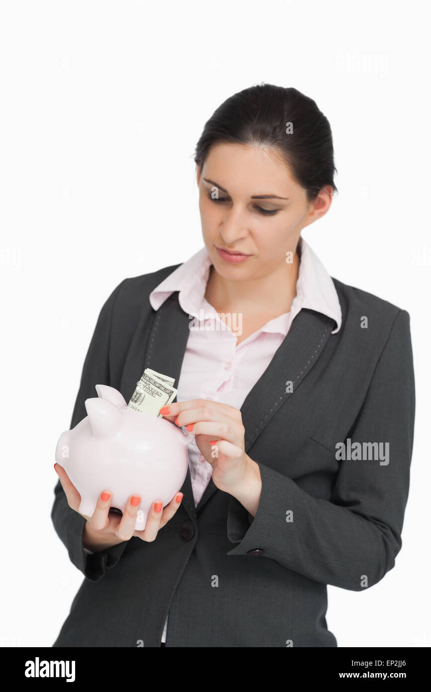 Bruna in tuta di dollari mettendo in un piggy-bank Foto Stock