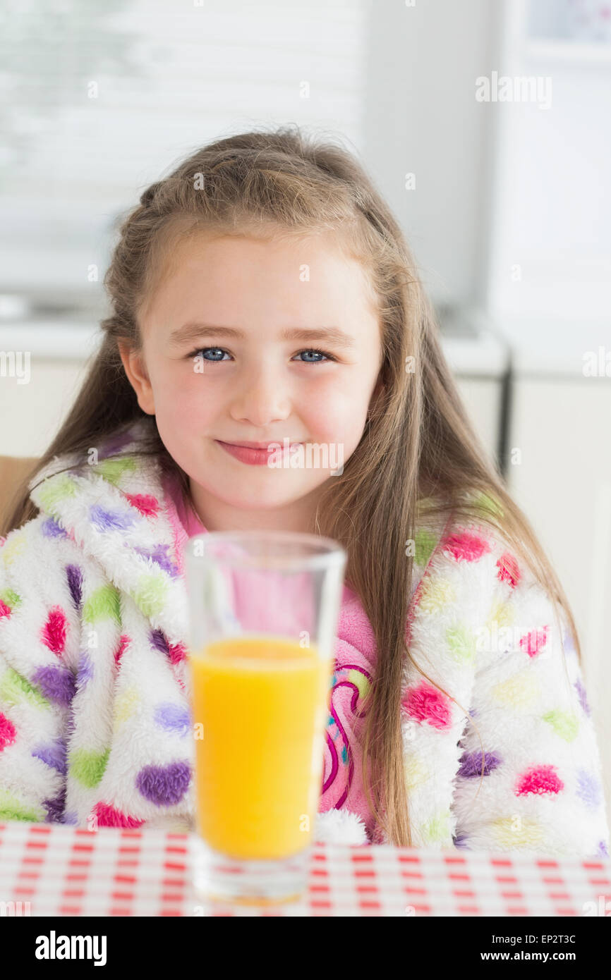 Poco ragazza seduta mentre sorridente con un bicchiere di succo di arancia Foto Stock