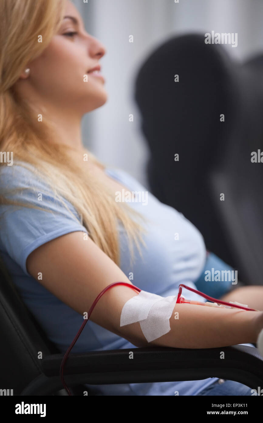 Donna sorridente ottenendo una trasfusione e seduto su una sedia Foto Stock