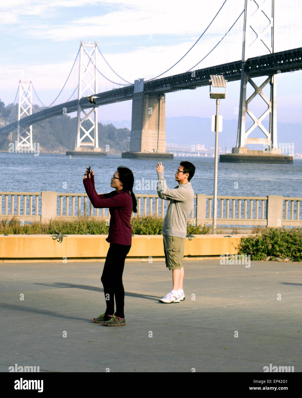I turisti che prendono selfie con i loro telefoni vicino al San Francisco Bay Bridge. Foto Stock