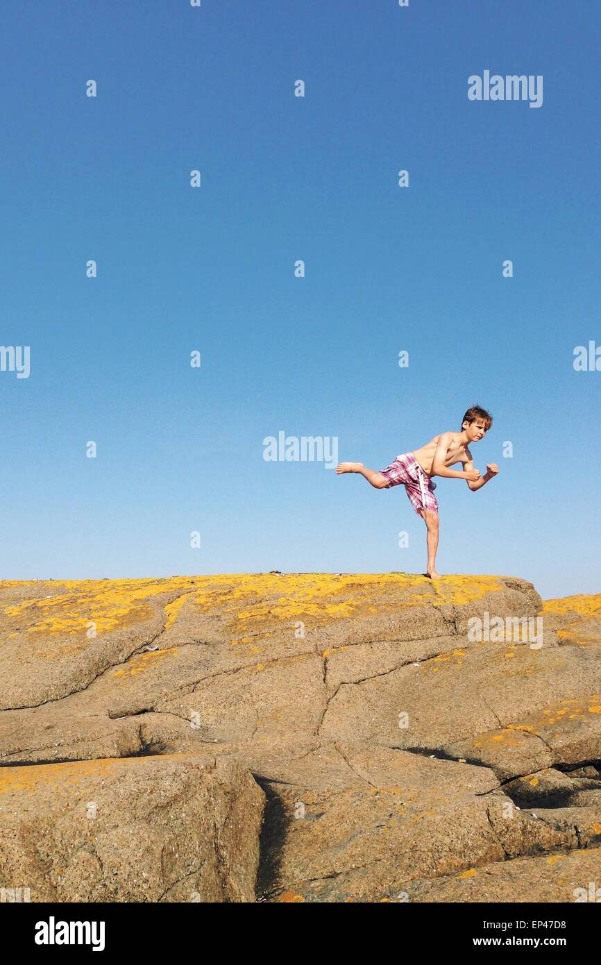 Ragazzo in piedi su una gamba sola su una roccia Foto Stock