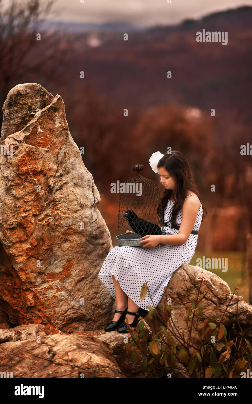 Ragazza seduta sulle rocce tenere una gabbia per uccelli con un ripieno a base black bird Foto Stock