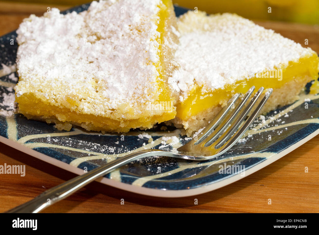 Lemon Bar che serve appena sostenuto e coperto di zucchero a velo. Servita su un blu e piastra bianca Foto Stock