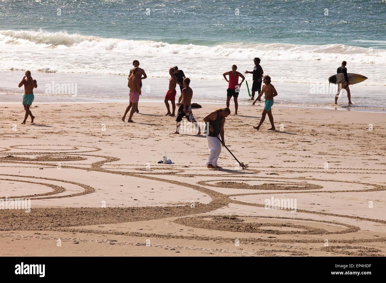 Le persone che giocano come qualcuno crea le opere in sabbia in Byron Bay, Australia Foto Stock