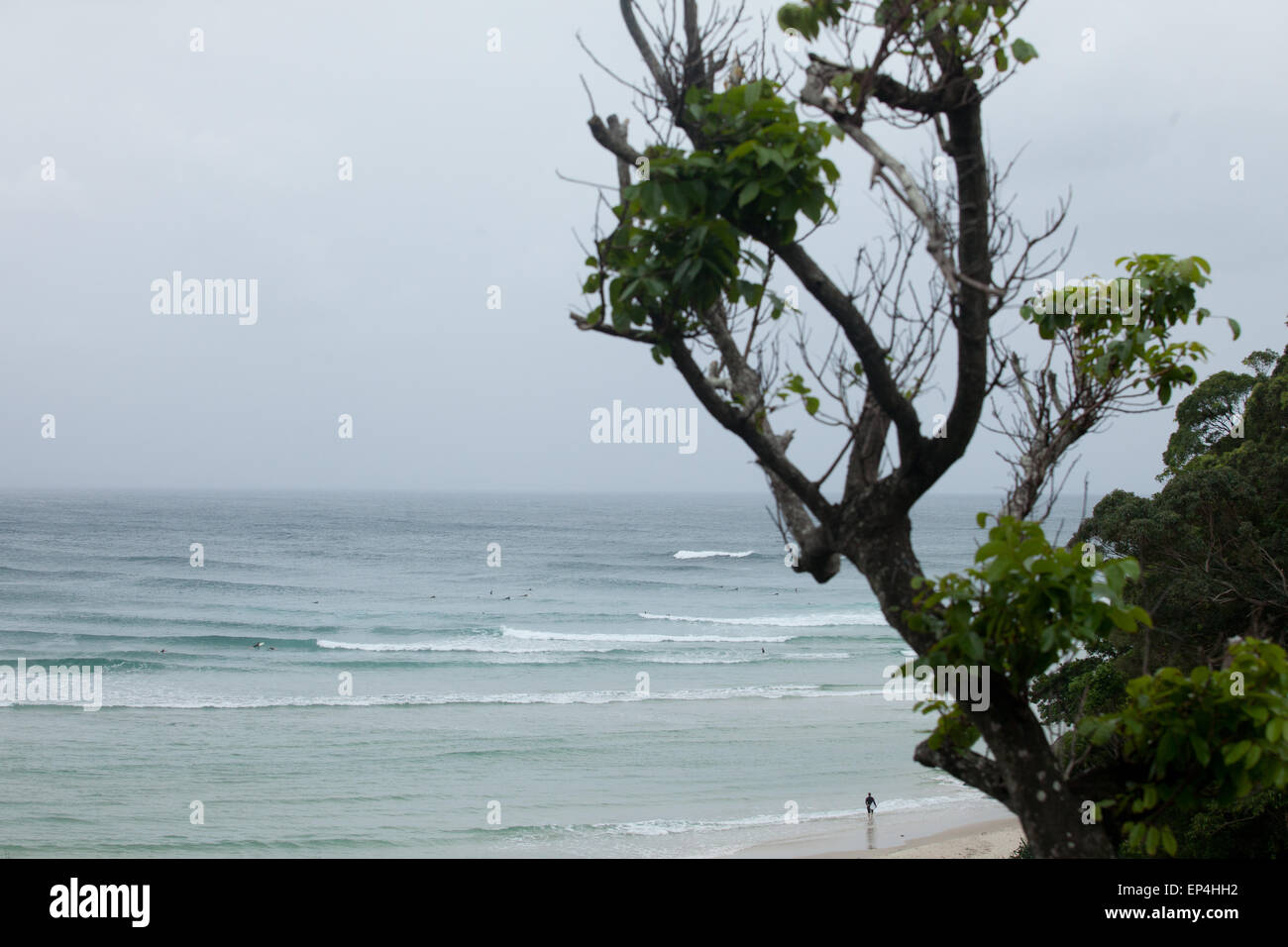 Una persona sorge sul litorale con una tavola da surf in mano affacciato sul surf in Byron Bay, Australia. Foto Stock