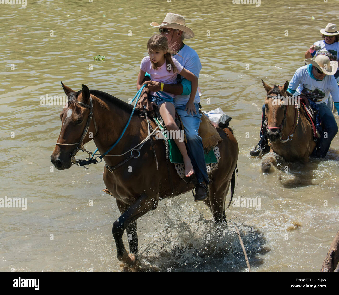 Cavaliere e figlia attraversando il fiume Pixaim a cavallo, Pantanal, Brasile Foto Stock