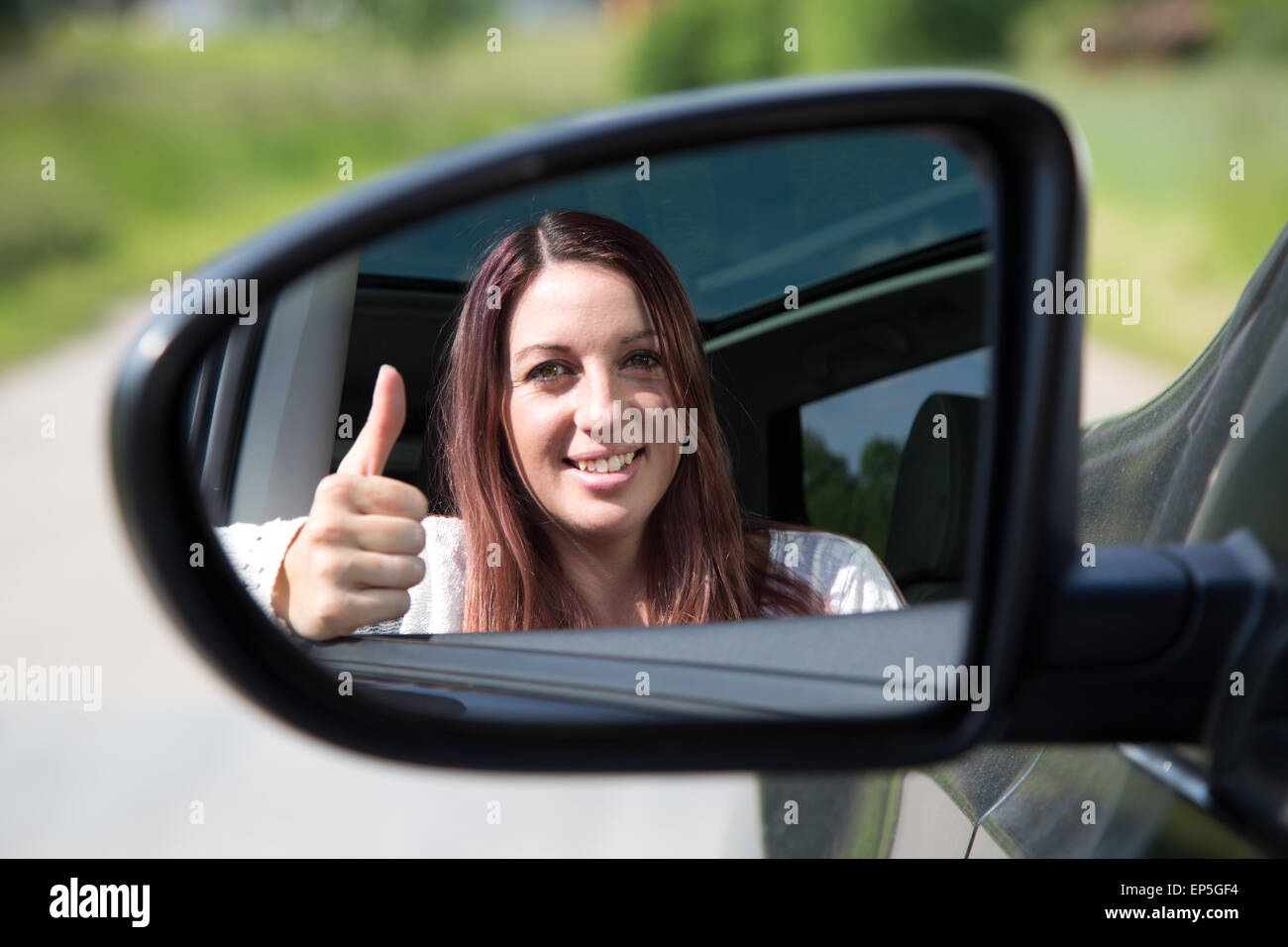 Autofahrerin zeigt Daumen hoch im Spiegel Foto Stock
